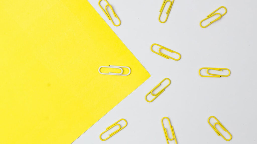 Yellow color paper clips with only a white one isolated on paper background